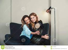 Two Pretty Young Women Sitting on Sofa and Looking To Mirror in Stock Photo  - Image of positive, happy: 124793678