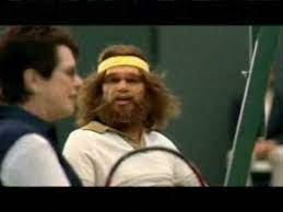 The geico caveman is sitting in a living room on a couch with a female companion. Geico Caveman Tennis Commercial Youtube