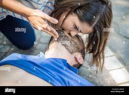 girl helping an unconscious guy with mouth to mouth resuscitation and cpr  Stock Photo - Alamy