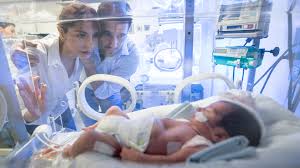 Newborn in a NICU incubator with parents nearby and clinical monitors