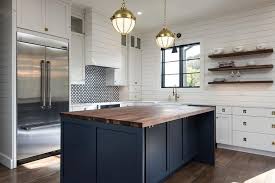 The rustic white shiplap accent wall contributes to the horizontal patterns found throughout the kitchen: Dark Blue Island With Walnut Countertop Transitional Kitchen