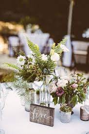 Rustic Wedding Centerpieces With Locally Grown Flowers And Ferns At A Woodla Flower Centerpieces Wedding Wedding Table Centerpieces Rustic Wedding Centerpieces