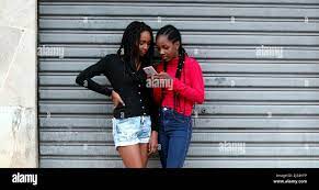 Candid black teens girls using cellphone, adolescent girl in shock  gossiping with friend Stock Photo - Alamy