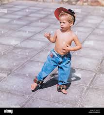 Children little white boy barefoot jeans shirtless cap scratching belly  looking away blonde cute suspicious expression emotion p Stock Photo - Alamy