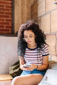 A Young Hispanic Woman Looking Down At Her Phone In A Cafe By Kristen Curette For Stocksy United Woman Looking Down Hispanic Women Curly Girl Hairstyles