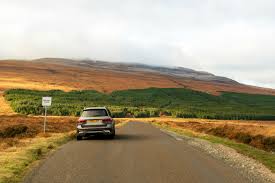 Placeholder image of a car driving on a scenic road through the Highlands.