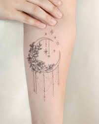 The moon is brightly colored with floral shapes and a single star hangs in the center. Moon Roses Tattoo On Inner Forearm