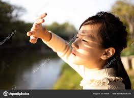 Asian child girl covering face by hand to protect,prevent face skin from  bright sun in