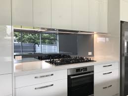 A white and gray marble countertop flanks a wolf range placed against mirrored backsplash tiles beneath a stainless steel hood accented with brass. Mirror Smoke Splashback Glass Splashbacks Kitchen Kitchen Mirror Modern Kitchen Design