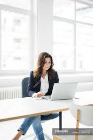Office woman sitting at desk. Smiling Businesswoman Sitting At Desk In Office And Working On Laptop Looking Down Self Employment Stock Photo 258093020