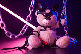 toy bear dressed in leather belts harness accessory for BDSM games on a  dark background in neon light - Gay Therapy LA