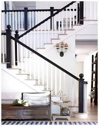 At the foot of a white staircase accented with a glossy black banister contrasting white spindles, a gold finial, and dark stained wood treads, a black and gold foyer chest is topped with framed art lit by a blue lamp. 18 Best Black And White Banister Ideas Banisters White Banister Home