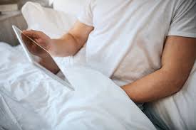 Guy se sienta en la cama por la mañana. sostiene la mano debajo de la manta  y se masturba. el hombre tiene una tableta blanca en la mano | Foto Premium