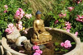 Brass Statue Of Lord Buddha In The Earth Touching Mudra Holding Begging Bowl Water Fountain Lotus Petals Rocks Pink Carpet Roses Tibetan Buddhist Style Buddha Garden Buddha Lotus Garden
