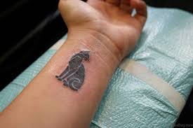 A silhouette of a black cat sitting on an intricately crescent moon. 31 Cute Cat Tattoos For Wrist