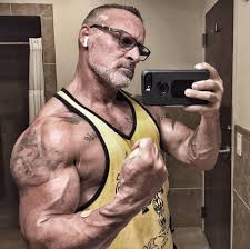 Muscular person in a yellow tank top taking a mirror selfie flexing arm muscle.
