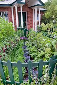 Front Entry Garden Of Brick House With Green Picket Curving Fence Vegetables Cabbages Carrots Beans He Planting Flowers Home Landscaping Edible Landscaping