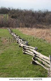 A few of the rails have been replaced with discarded branches, giving the fence a very rustic look. Stock Photo A Split Rail Fence Runs Down A Hill Next To A Field To A Streambed Then Up A Hill In The Distan Rustic Fence Split Rail Fence Landscaping Fence
