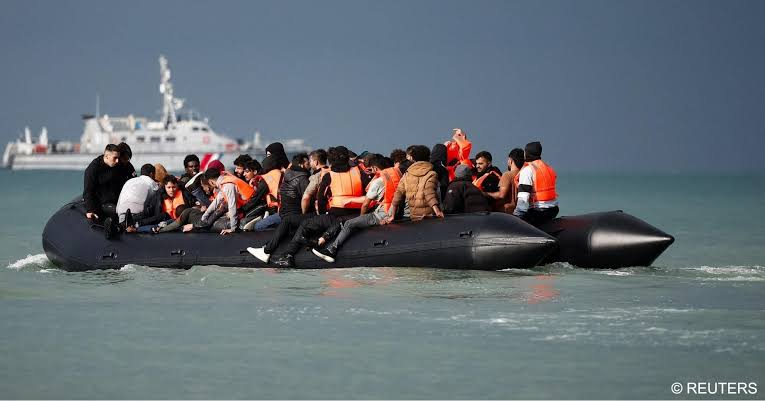 📸 A man jumping off an inflatable dinghy as it leaves the shore. People  waist-deep in water, hoping to make it onto a boat already carrying more  people than is safe. These