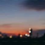 A blurry photo of the sun setting behind a building photo ...