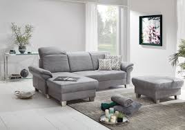 Wanita duduk di sofa sambil melihat ponsel dengan laptop di pangkuan. Ponsel Studioline Polsterecke Hellgrau Mobel Letz Ihr Online Shop