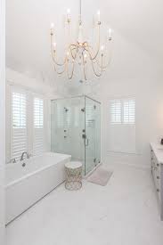 An Antique Brass Chandelier Hung From A Vaulted Ceiling Lights A Bathroom Boasting A Round Marble T Glamorous Bathroom Simple Bathroom Antique Brass Chandelier