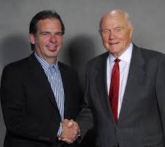 Two men shaking hands in front of a gray background. John glen american  hero astronaut.