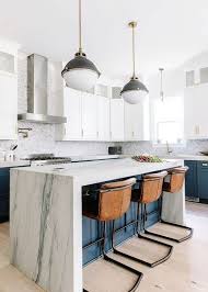 White dome lights hang over a white quartz waterfall countertop accenting a light gray island seating four dwr master barstools facing a stainless steel sink with a polished nickel gooseneck faucet mounted beneath a window. 30 Waterfall Kitchen Countertops With Pros And Cons Shelterness