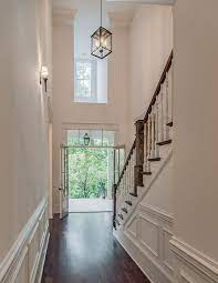 A Hallway Lined With White Wainscoting Leads To An Elegant Two Story Foyer Boasting Glass Paned Double Foyer Lighting Foyer Decorating Dark Stained Wood Floors