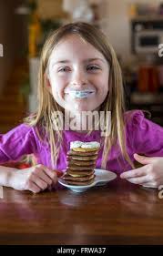 Portrait of happy girl avec de la crème chantilly sur ses lèvres et une  pile de crêpes au chocolat mini Photo Stock