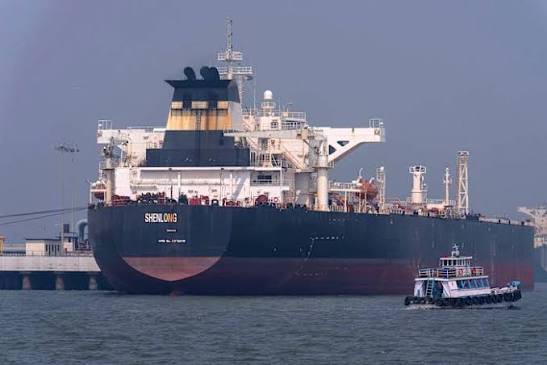 A commercial cargo ship navigating the narrow Strait of Hormuz amid increased naval presence.