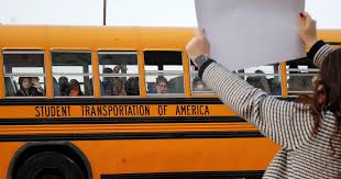 Bussed students stare out the windows to witness the commotion raised by  their teachers and community