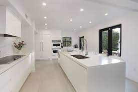 The classic white luxury kitchen features a wooden coffered ceiling, wide plank flooring, central island with black marble countertop and a breakfast bar lined with wooden stools. Luxury White Kitchen Cabinets Design Close Esc