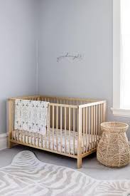 Lovely Blue Gray Nursery Is Furnished With A Blond Wood Crib Placed Beside A Woven Basket On A Gray Rug Lay Nursery Paint Colors Wood Nursery Blue Gray Nursery
