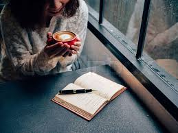 Woman holding a coffee cup by the window with a book