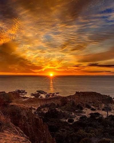 TORREY AMBER SKY - This breathtaking sunset over Torrey Pines captures the dramatic coastal cliffs and rugged terrain. Golden sunlight pierces through spectacular cloud formations over the Pacific Ocean. The image showcases