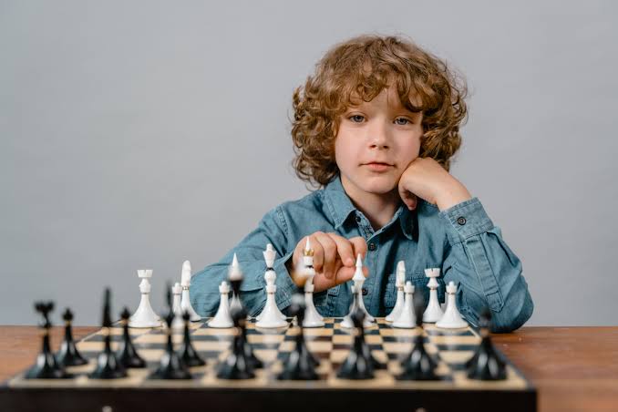 Young child learning chess openings for beginners at a wooden chessboard