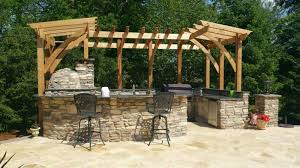 U shaped outdoor kitchen is fitted with stainless steel cabinets and concrete countertops accompanied by an outdoor pizza oven, bbq and outdoor sink shaded by a pergola. Outdoor Kitchen With Seating And Pergola Millenium Stoneworks