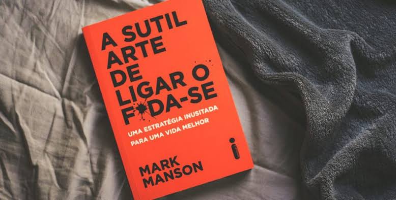 Livro A Sutil Arte de Ligar o F*da-se aberto sobre uma mesa de madeira no Refúgio Aurora