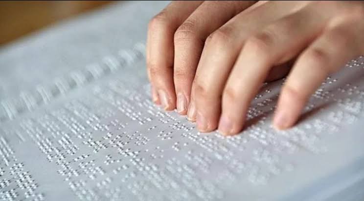 Dos manos sobre un folio en blanco escrito en braille