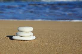 three white stones on the sand near the ocean water.
