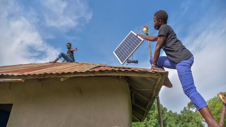 Young African boy installing solar panel on a local roof