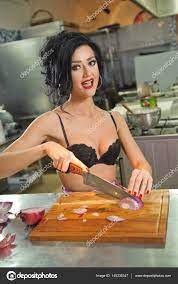 Mujer hermosa y sexy en la cocina. Morena sonriente preparando comida.  Chica joven con sujetador negro