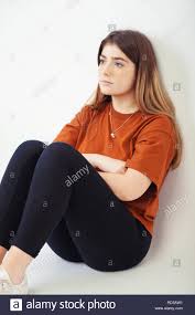 Blonde Teenage Girl Sitting Down With Her Back Against A White Wall Stock Photo Alamy