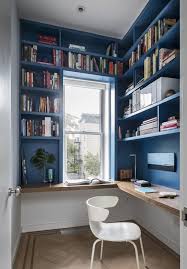 A bright and eclectic home office with a navy a chic blue home office, all the walls taken by storage units, a blue desk, a black chair and a catchy chandelier with candles. 25 Chic Blue Home Offices In Various Styles Shelterness