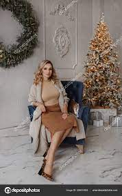 Beautiful sexy young blonde woman in stylish clothes sitting in an armchair  near the Christmas tree in the interior decorated for New year celebration  Stock Photo by ©innarevyako 508424954