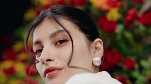 Elegante retrato de una mujer de cabello oscuro, con pendientes de perlas,  posando frente a vibrantes flores rojas y amarillas. Mujer confiada posando  con un fondo floral vibrante 811577444