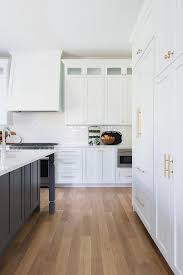 Stacked White Shaker Cabinets Adorned With Brass Hardware And Fixed Beside A White Wood Paneled White Wood Paneling White Oak Hardwood Floors Oak Floor Kitchen
