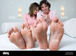 Couple sitting on a bed, smiling for the camera, barefoot in foreground  Stock Photo - Alamy