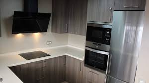 Cocina con gabinetes interiores en melamina blanca, con gabinetes superiores de 65 cms, en color blanco al alto brillo con puertas de vidrio esmerilado y marcos de aluminio. Cocina Dica En Color Madera Para Una Joven Pareja